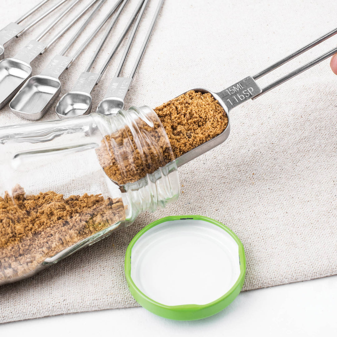 Stainless Steel measuring spoon scooping spices on a textured grey surface. 