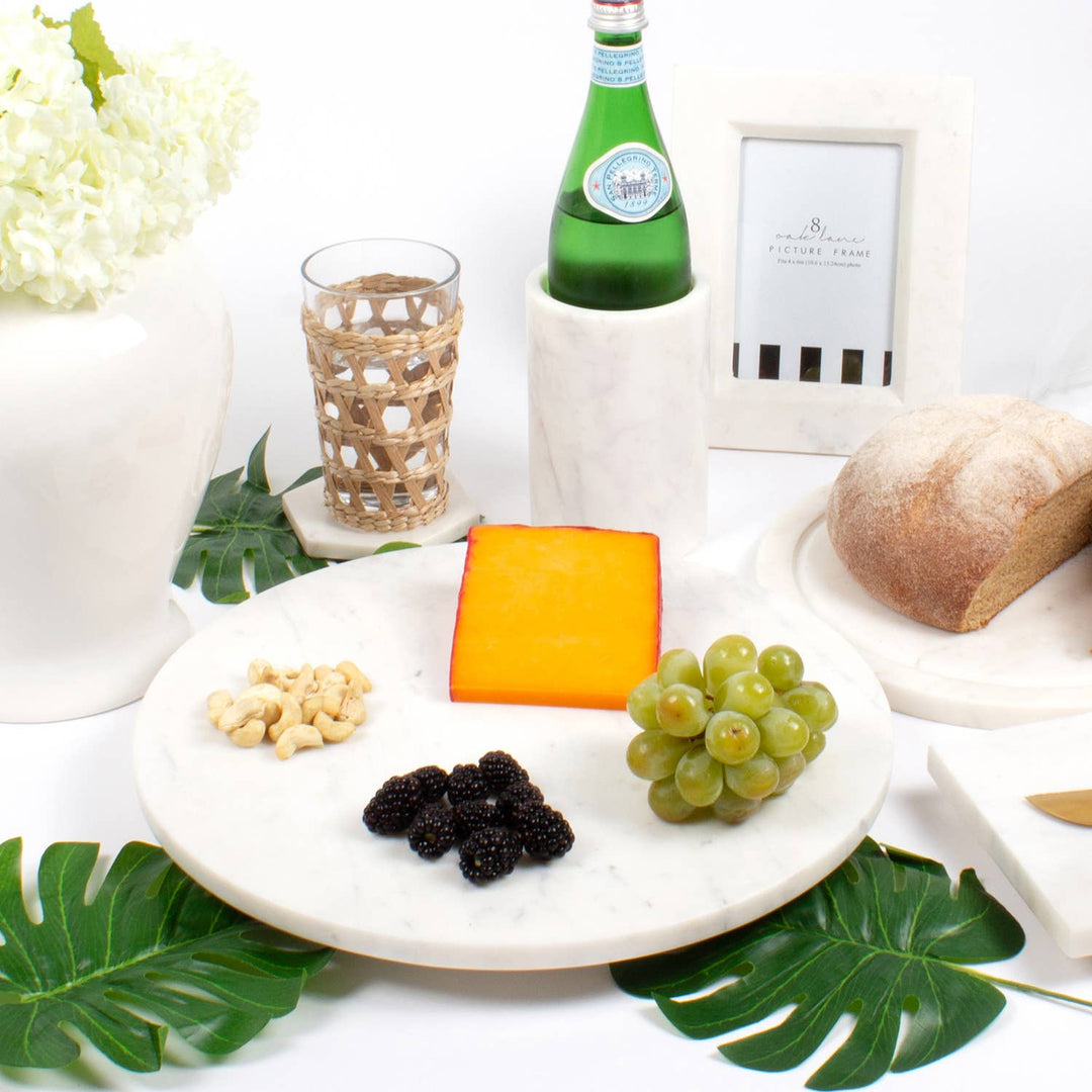 Platter with cheese, grapes, and nuts on a table with a bottle of wine in a cooler and bread.