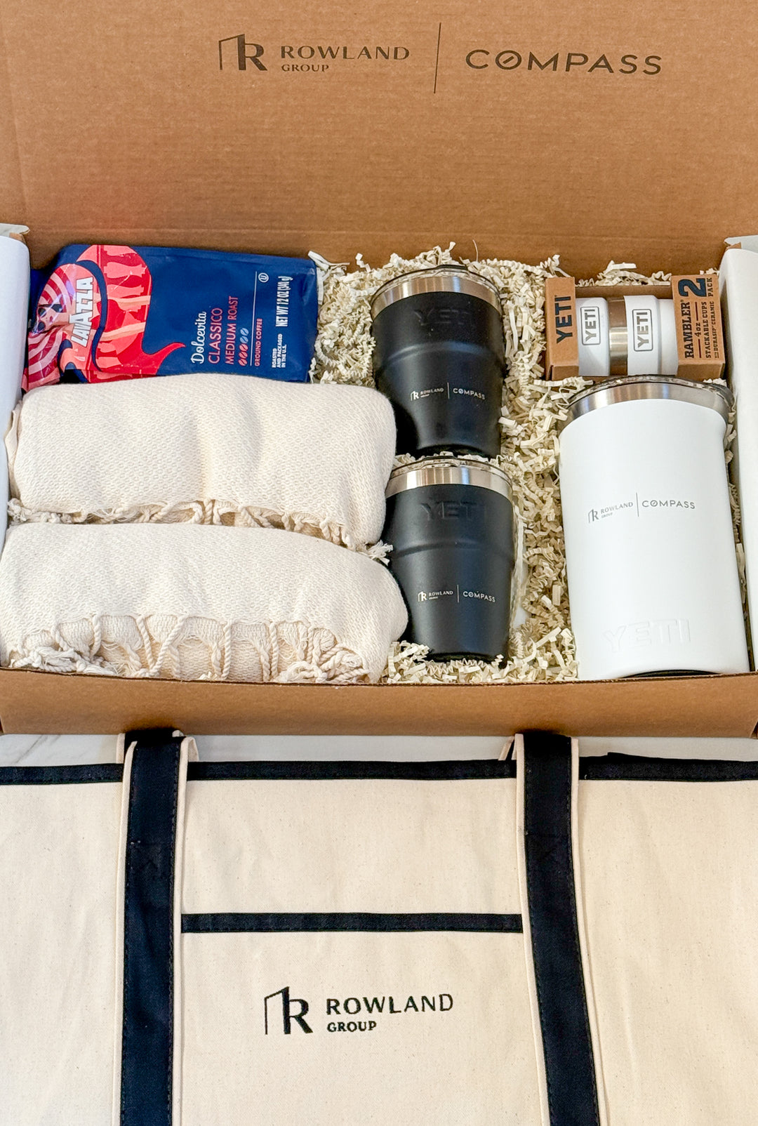 Gift set with Rowland Group branding including tumblers, coffee, blankets, tote, press and other items.