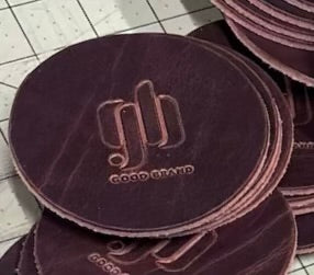 Brown leather coasters with "Good Brand" logo and text on a tiled floor background