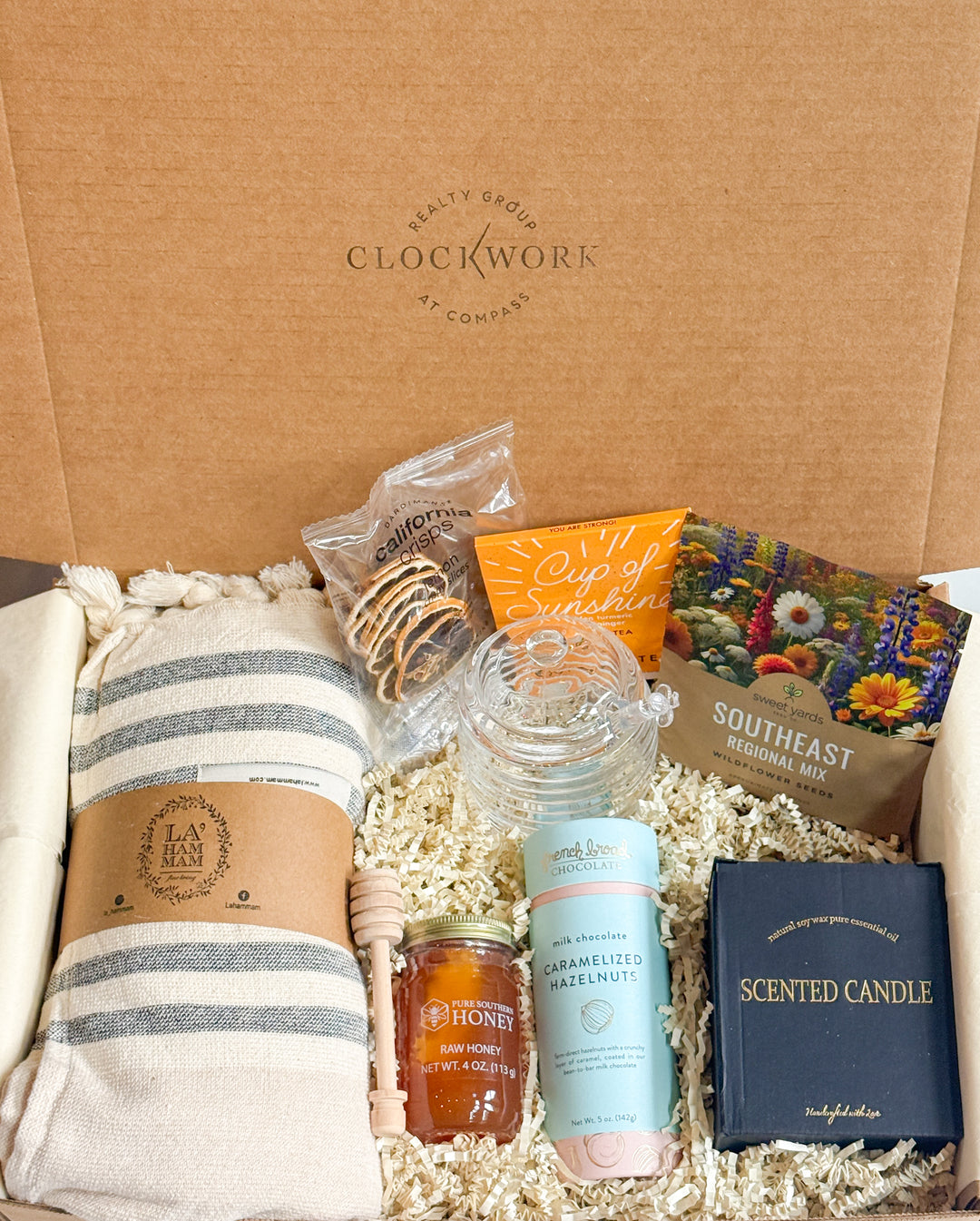 Gift box with various items including a candle, snacks, and a blanket, branded &
