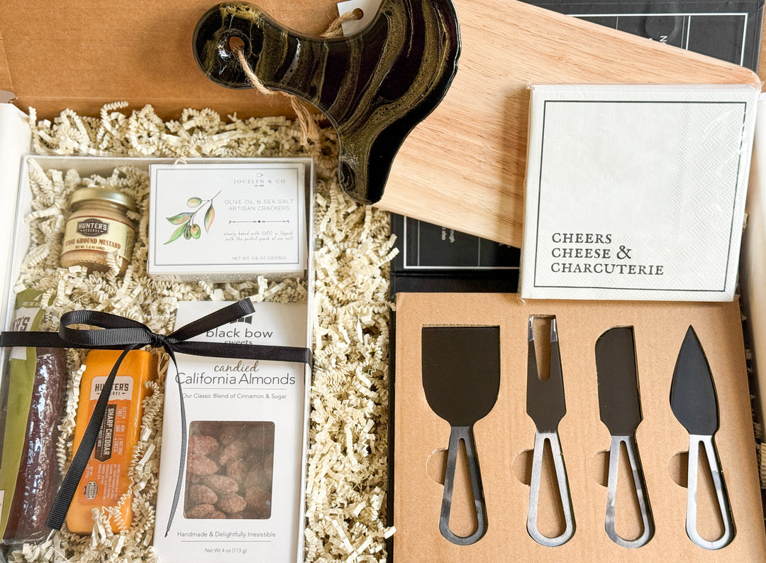 Gift set with charcuterie items, and cheese board and knives in a wooden box.