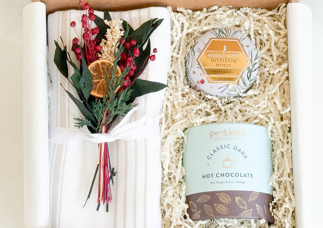 Gift set with classic hot chocolate, a hand towel, a small flower bouquet, and a small candle in a box.