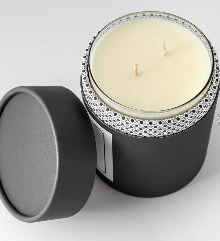 Candle in a black container with decorative lid on a light gray background