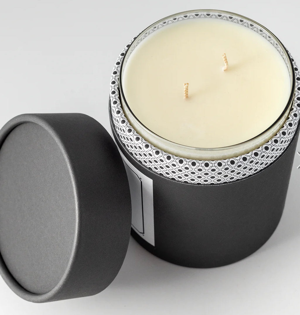Candle in a black container with decorative lid on a light gray background