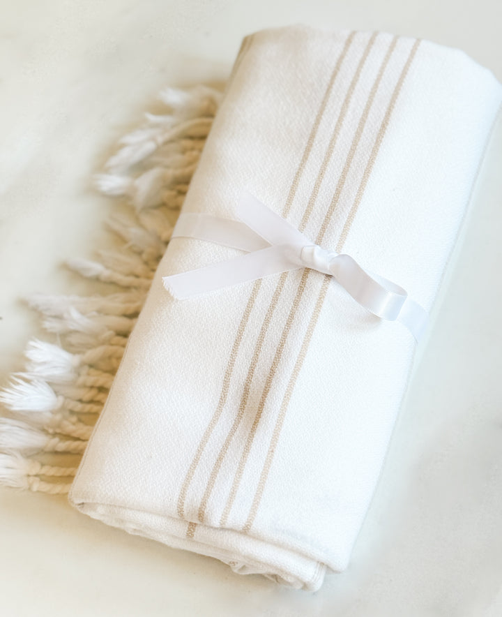 Folded white towel with beige stripes and a ribbon on a light background