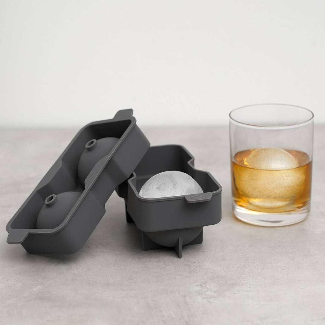 Gray silicone ice cube tray with a glass of whiskey and ice cubes on a light surface