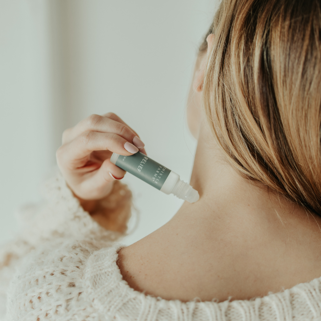 Person applying a essential oil roll-on product to their neck with a dropper bottle.