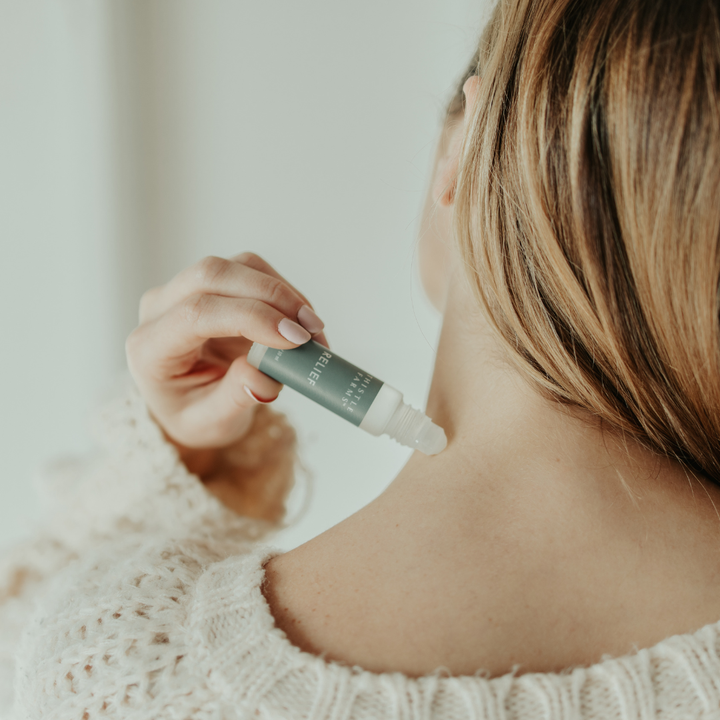 Person applying a essential oil roll-on product to their neck with a dropper bottle.