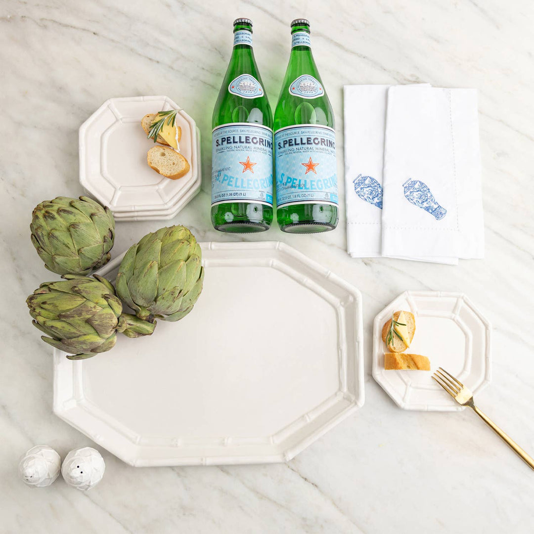 Two bottles of S.Pellegrino on a marble surface with artichokes, white dishes, salt and pepper shakers and lemon slices.
