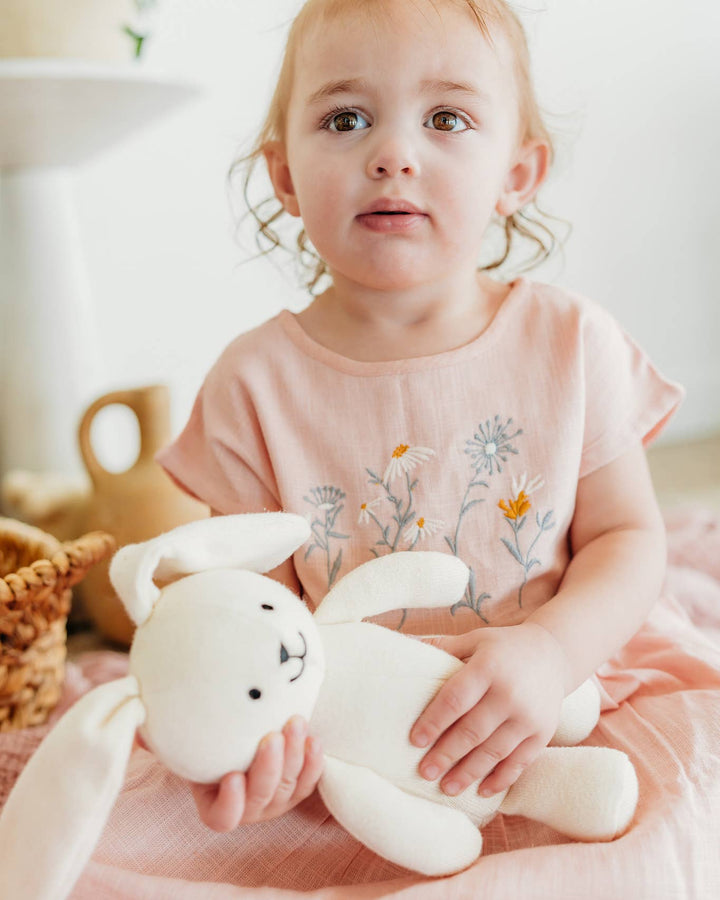 Child holding a white plush toy in a softly lit room