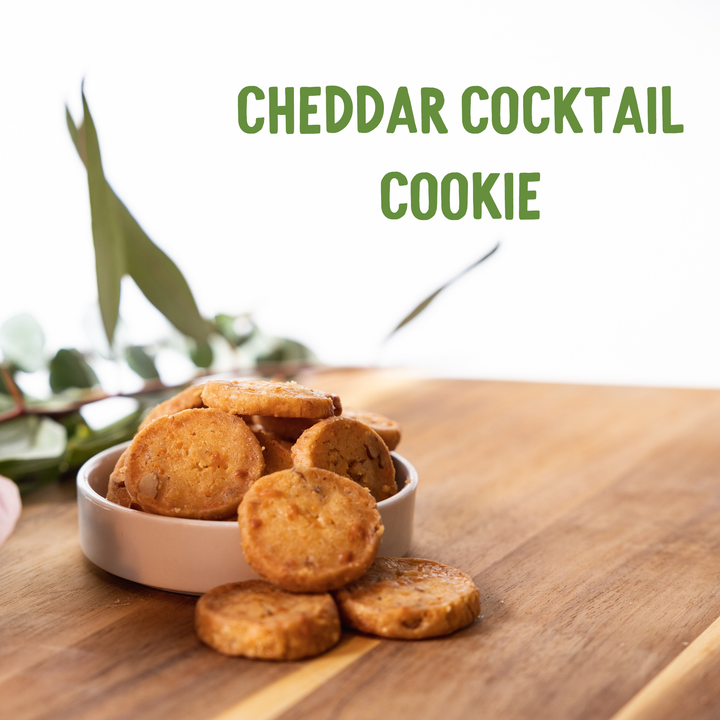 Cheddar cocktail cookies in a white bowl on a wooden surface with greenery in the background.