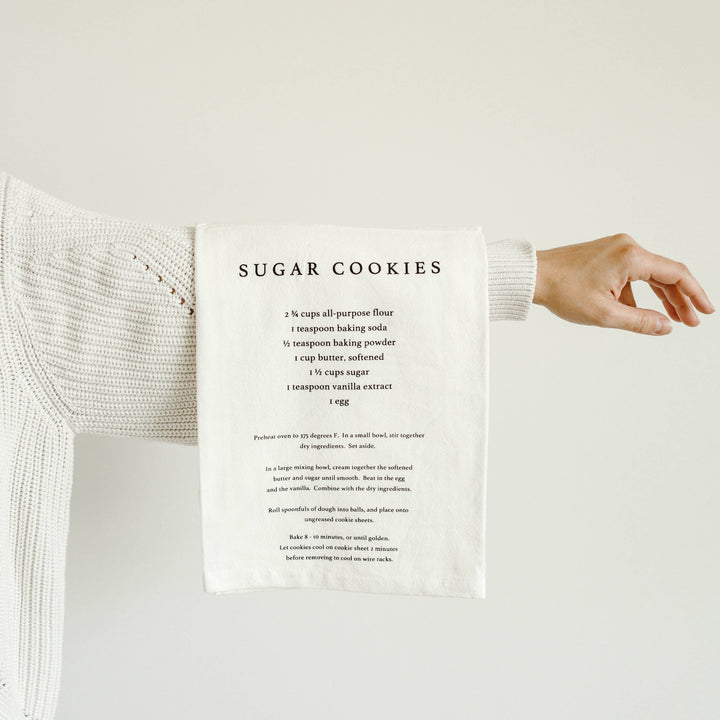 White towel with sugar cookie recipe printed on it, held by a person wearing a white sweater.
