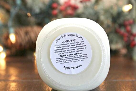 White candle with a warning label on a wooden surface with blurred decorative background