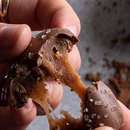 Close-up of a hand holding a partially eaten chocolate truffle with a blurred background.