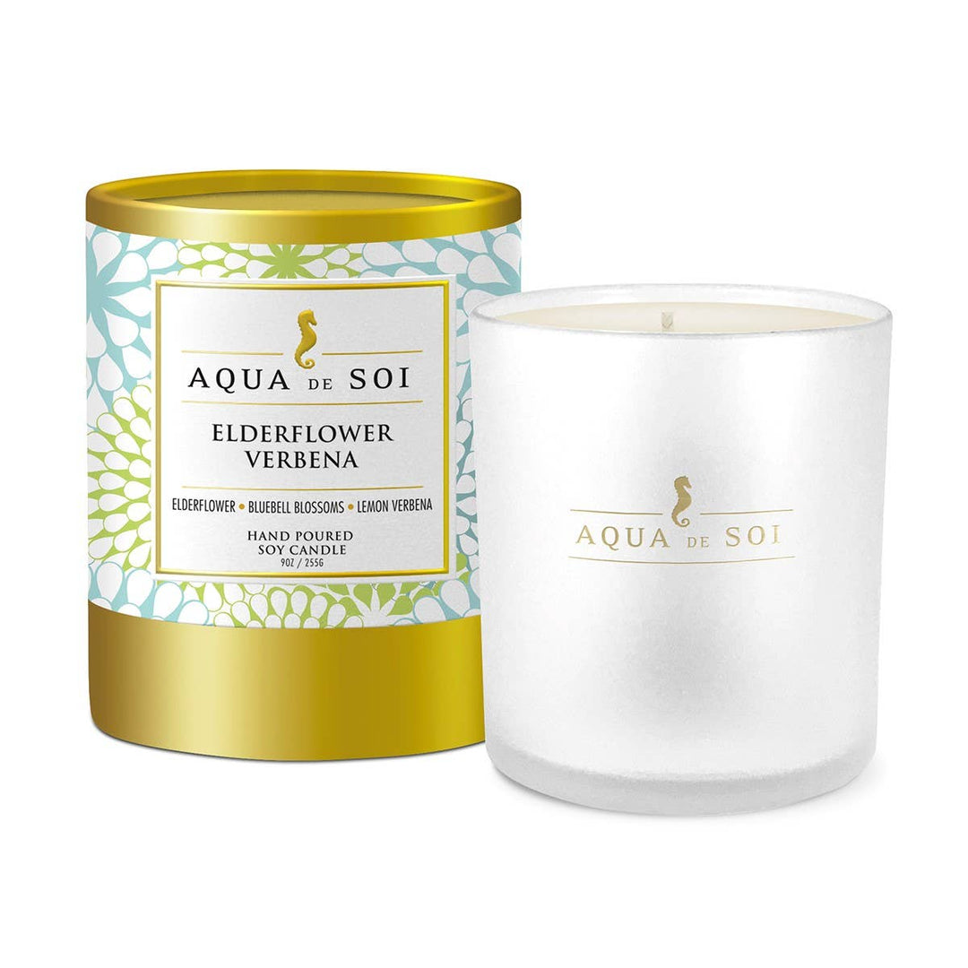 A boxed candle with the label 'Aqua de Sol Elderflower Verbena' on a white background with gold accents, and a clear glass candle container with a white label.