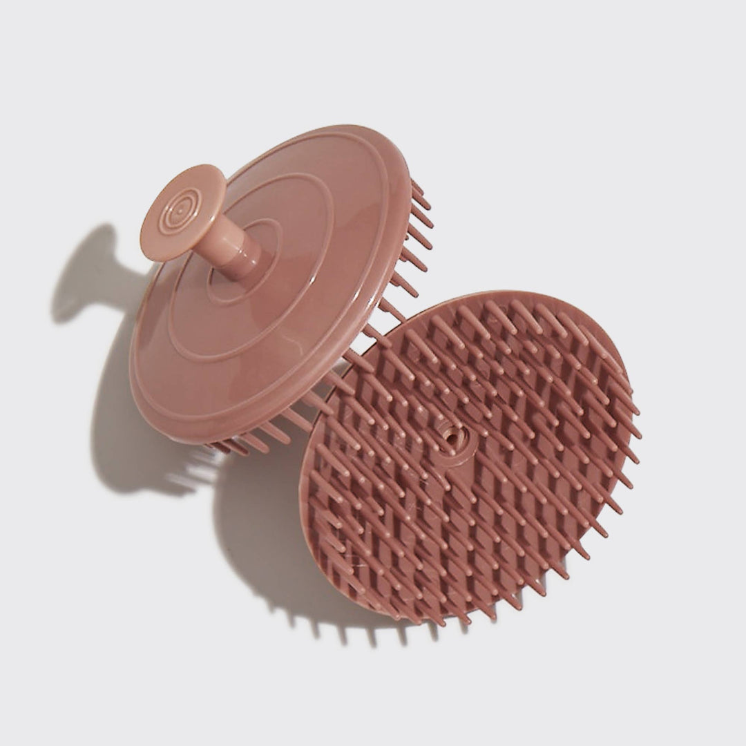 A terracotta-colored, plastic scalp exfoliator with flexible bristles on a white background. 