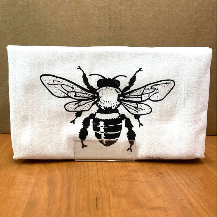 White pouch with a black bee design on a wooden surface and brown background