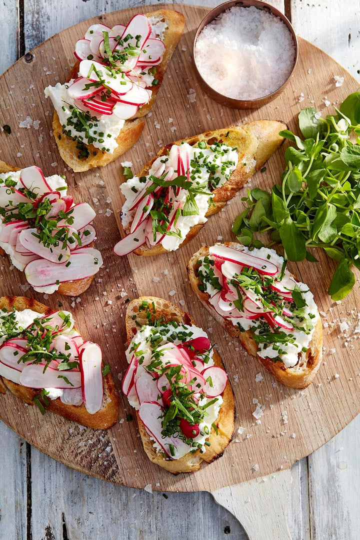 Plated bruschetta with radishes and herbs on a wooden board and a cup of salt.