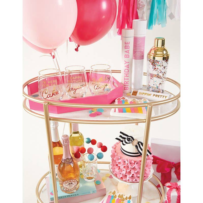 Decorative bar cart with birthday-themed items including glasses, bottles, and balloons.