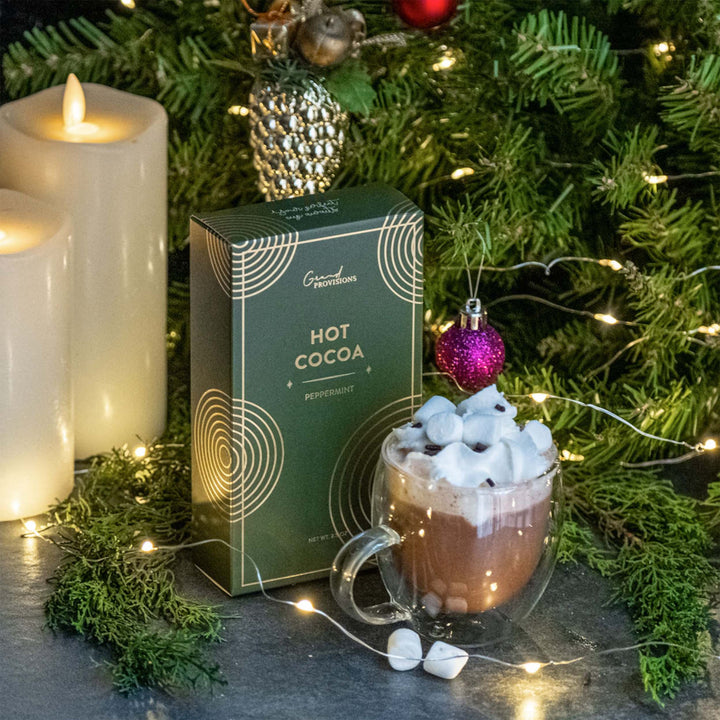 Hot chocolate with marshmallows, a box of hot cocoa, and Christmas decorations on a table.