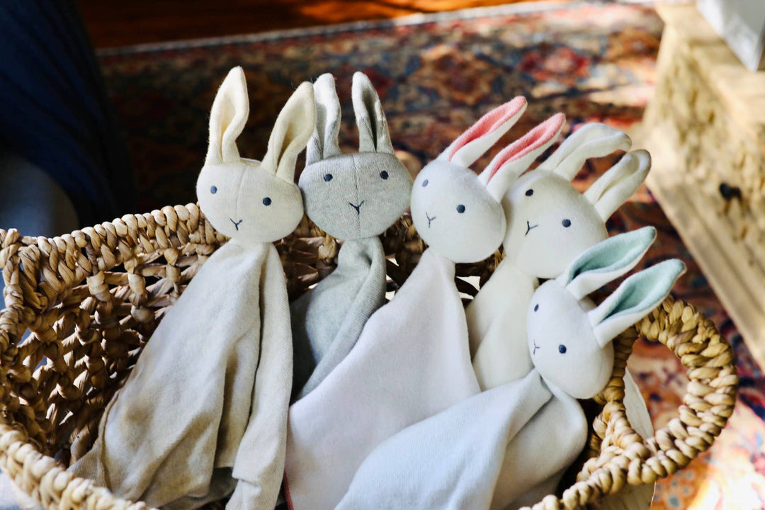 Set of plush rabbit toys in a woven basket on a textured surface
