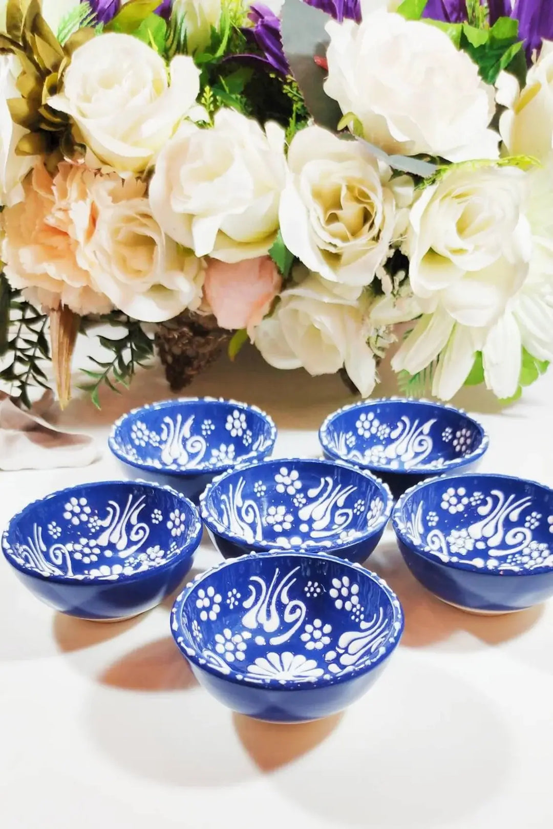 Set of blue ceramic bowls with floral patterns on a white surface, with flowers in the background.