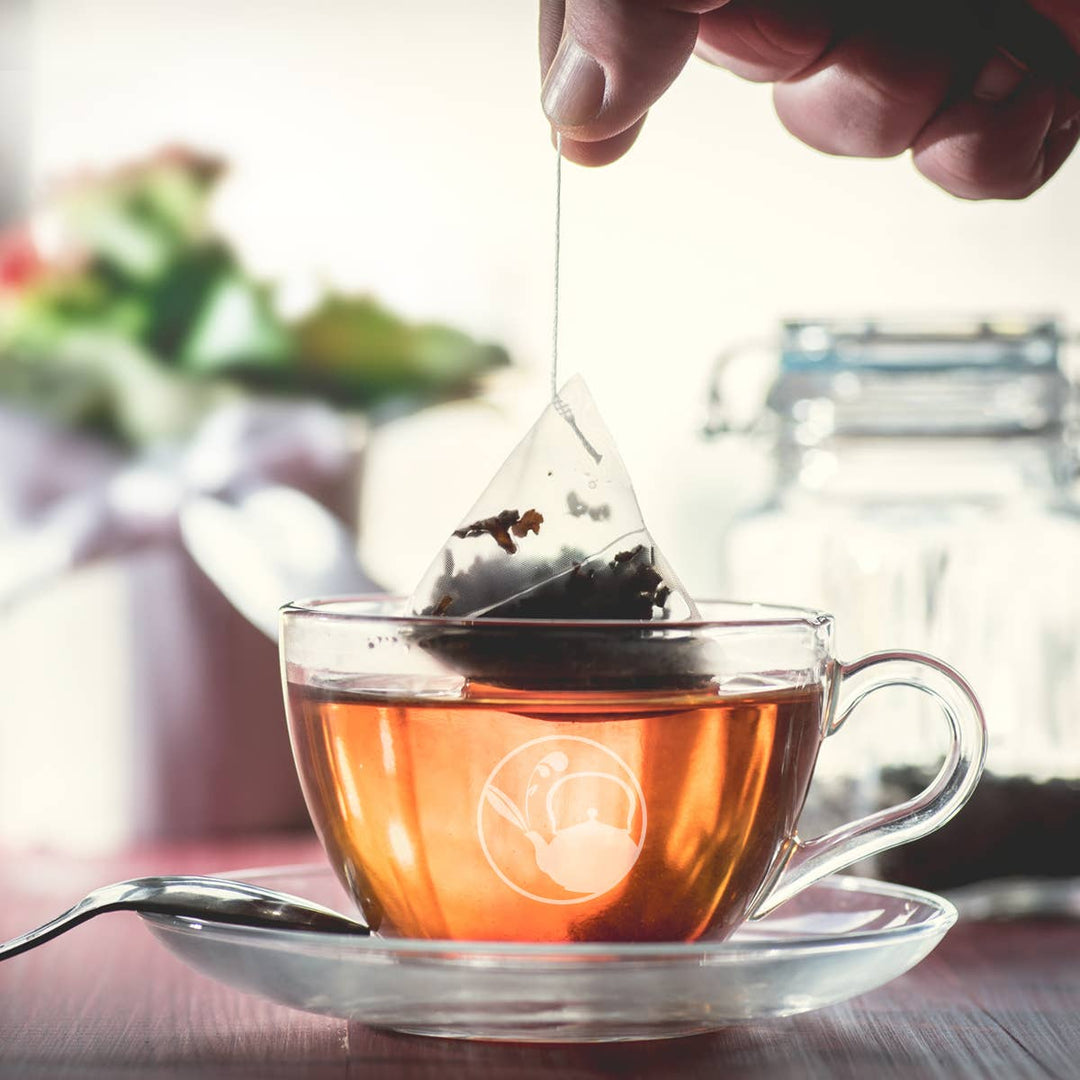 Tea bag being added to a glass cup of tea on a blurred background