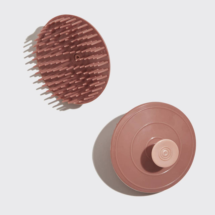 A terracotta-colored scalp exfoliator with flexible bristles on a white background. 