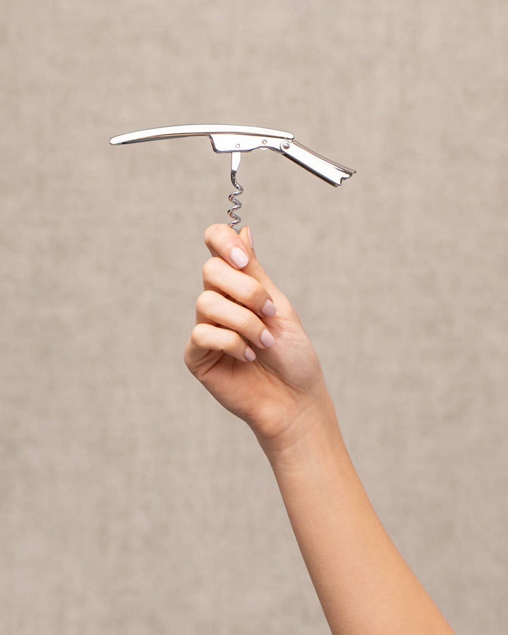 Hand holding a silver corkscrew against a beige background