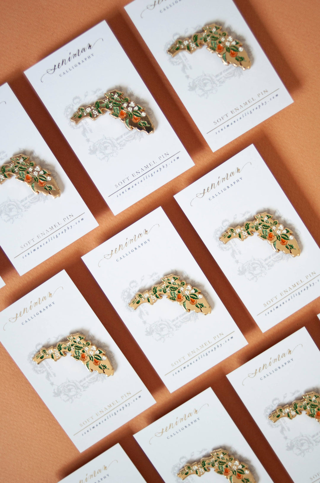 Decorative brooches on white cards with gold text on a brown background