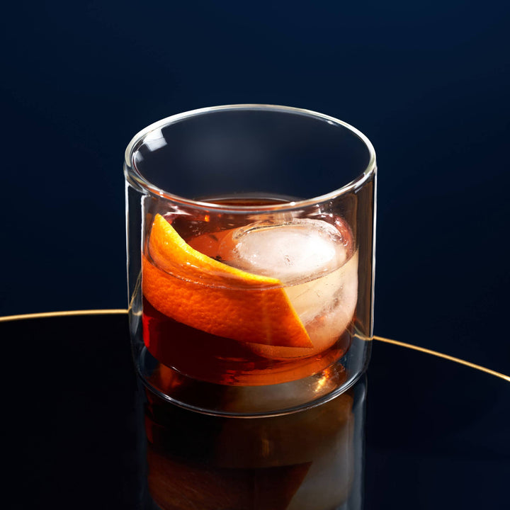 Glass of cocktail with orange slice and ice cube on a dark background