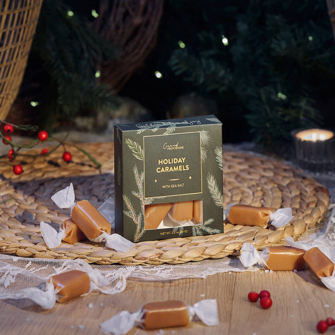 Box of Holiday Caramels with sea salt on a woven mat with a Christmas tree in the background