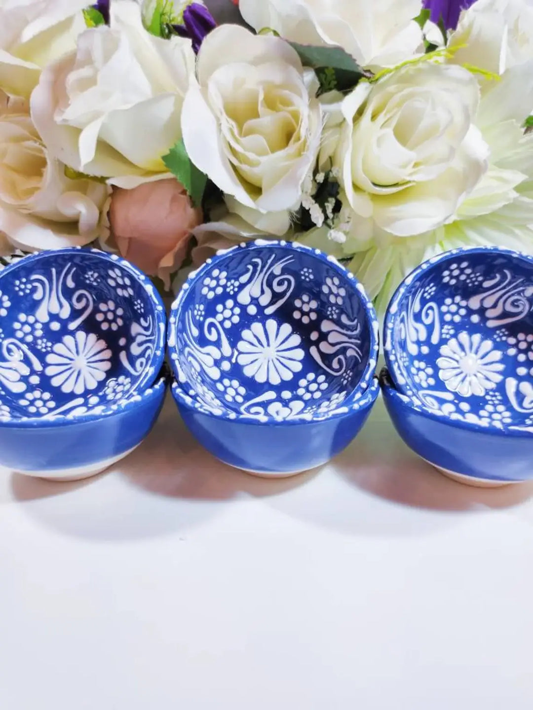 Three blue ceramic bowls with white floral patterns in front of a bouquet of flowers.