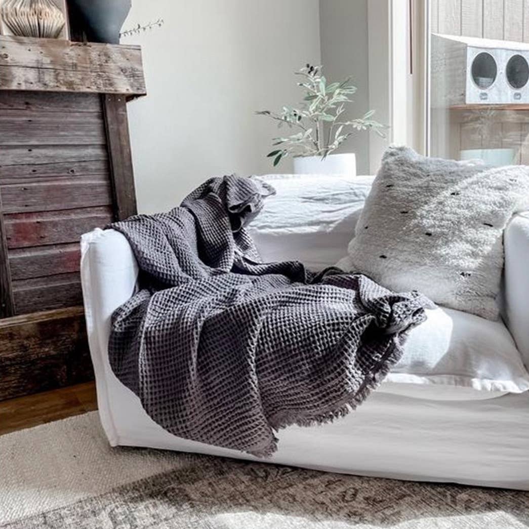 White sofa with a dark gray textured throw blanket in a cozy living room setting.