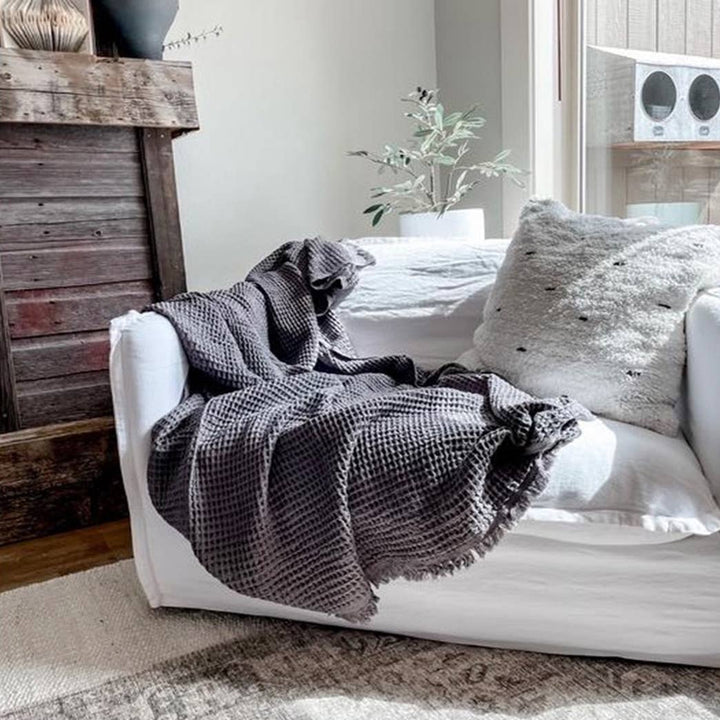 White sofa with a dark gray textured throw blanket in a cozy living room setting.