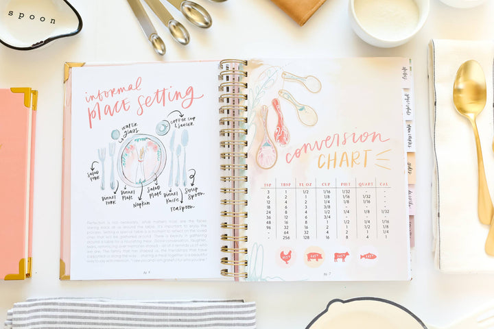 Open spiral-bound notebook with kitchen-themed pages on a white surface with kitchen utensils.
